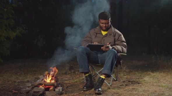 African Traveler Working on Tablet Pc By Campfire