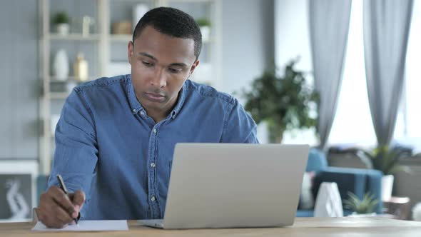 Young African Man Writing on Documents in Office