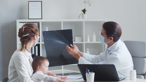 Male pediatrician is examining little baby. Doctor, mother and daughter in medical office.