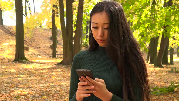 A Young Asian Woman Works on A Smartphone in A Park