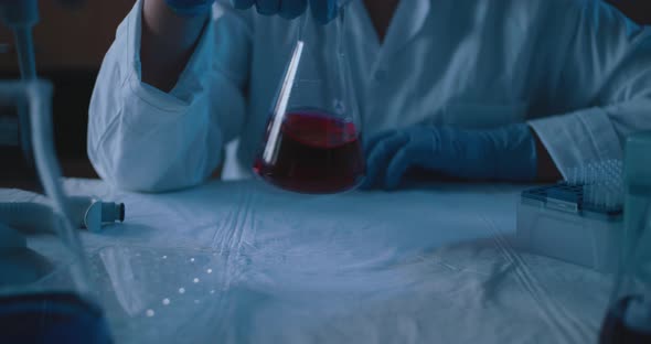 Female research scientist mixing up a conical flask with red liquid, slow motion