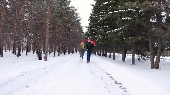 Young Couple Holding Hands Together While Running Away with Red Heart Shape Balloons