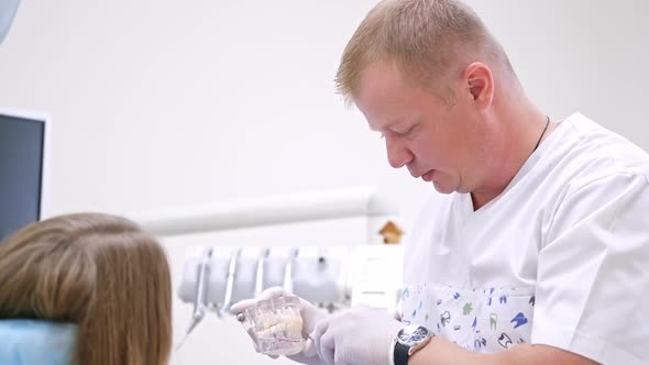 Doctor shows his young blonde woman patient on a plastic jaw sample how he will treat her teeth.