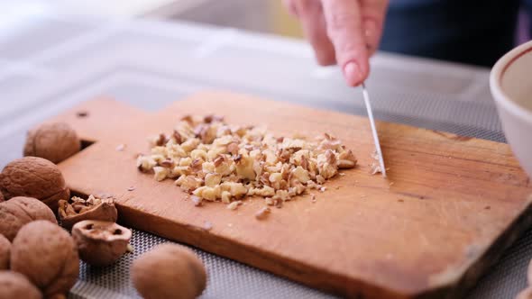 Chopping Walnuts Cores with Kitchen Knife on a Wood Cutting Board