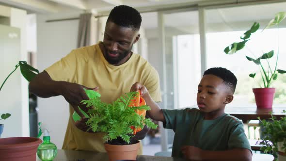 African american father and son watering plant pot together at home