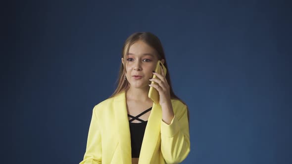 A Young Teenage Girl Talking on the Phone Against a Blue Background