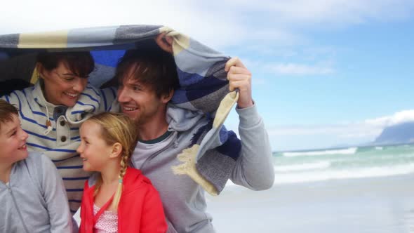 Happy family hiding in blanket at beach