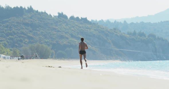 The Handsome Man with a Perfect Athletic Body in Swimming Trunks Having Fun on a Deserted Beach in