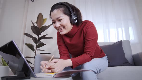 Asian woman on redshirt using a tablet with headphone for meeting online at home