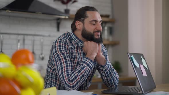 Satisfied Successful Handsome Middle Eastern Man Sitting in Kitchen with Laptop Smiling