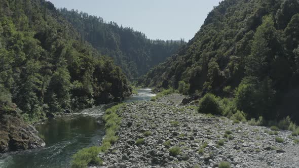 Slow drone flight over a rocky river surrounded by lush forest