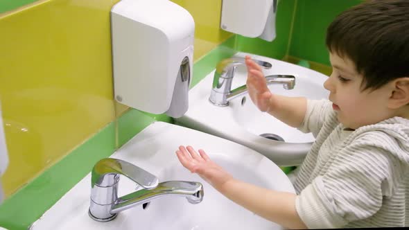 A Preschooler Child Puts His Hand Under a Soap Dispenser Soaps His Hands