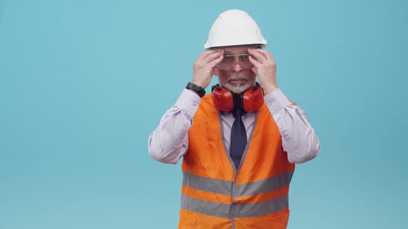 Adult Man Engineer with a Helmet and Work Vest Puts on Protective Glasses and Folds Arms on Chest in