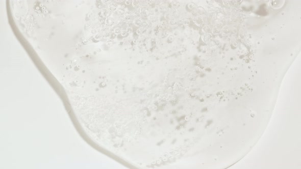 Macro Shot of Transparent Cosmetic Fluid Gel Cream With Bubbles Flowing Down on a White Surface