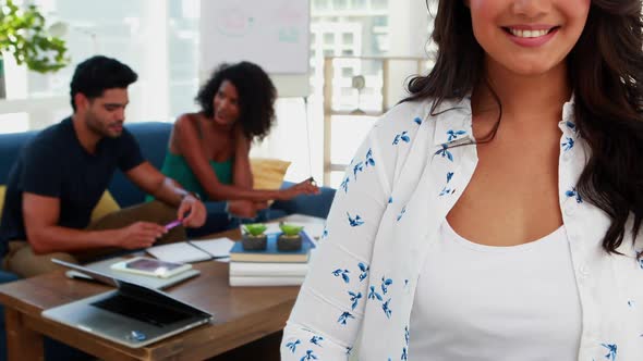 Smiling female executive standing in office while colleague discussing in background 4k