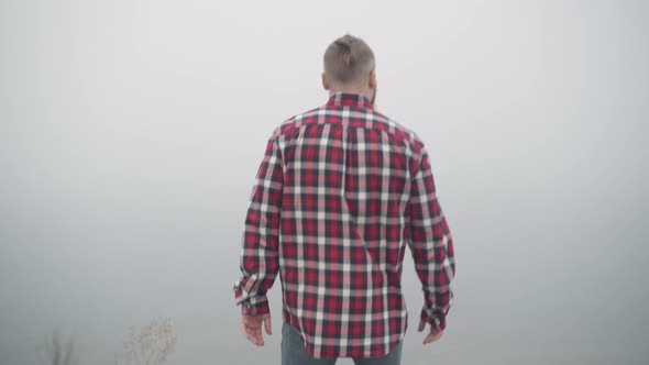 Young Man Walking to River Bank on Cloudy Foggy Day Stretching Hands Breathing in Fresh Air