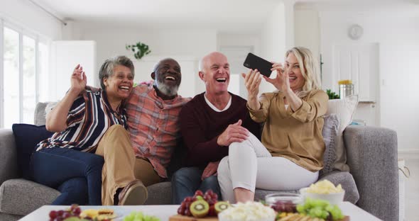 Two diverse senior couples sitting on a couch using a smartphone and laughing