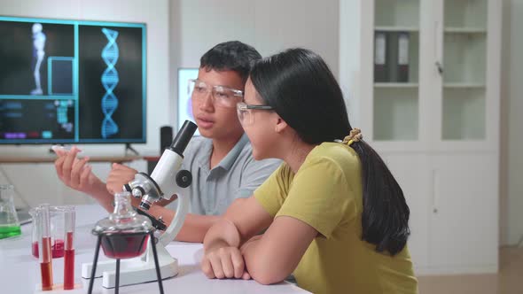 Asian Boy And Girl Learning Science Experiment In Laboratory At Classroom. They Are Talking Together