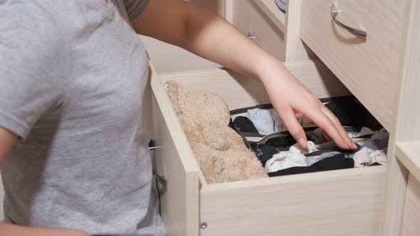 Woman Chooses Socks in Drawer of Large Cabinet in Room