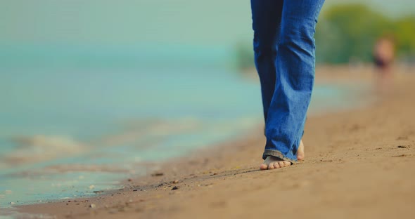 Woman in Wet Jeans and Bare Feet Walks in the Sand on the Beach