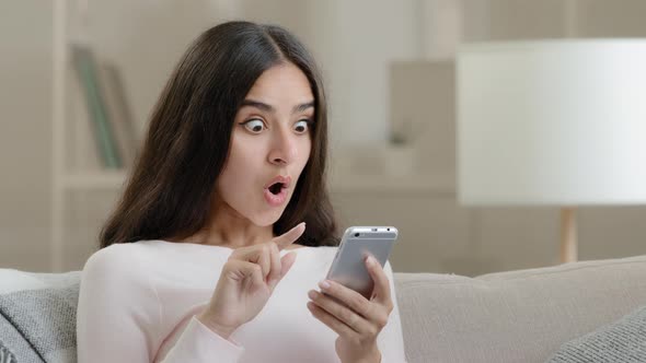 Amazed Pretty Arab Woman Girl Scrolling Pictures Likes Selfie Photos on Phone Using Mobile Options