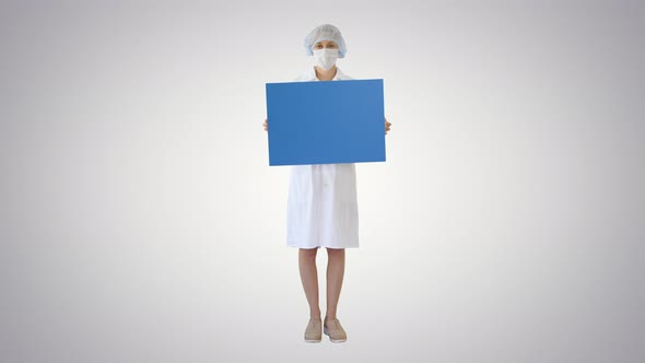 Young Woman Doctor in a Mask Holding an Empty Bill Board on Gradient Background