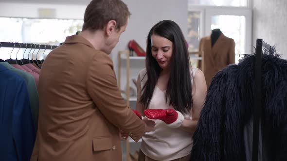 Joyful Happy Woman Trying on Red Mittens Smiling Looking at Camera As Blurred Cheerful Gay Man