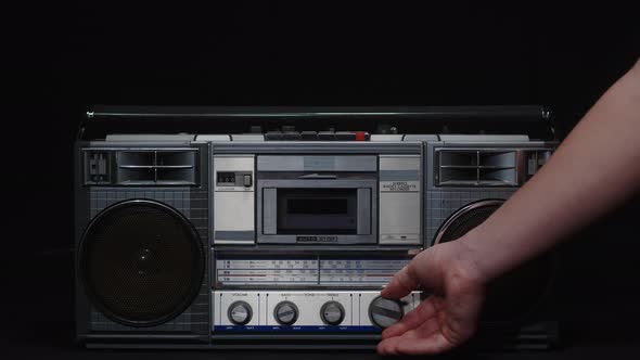 A Man's Hand Turns the Frequency Adjustment Knob of an Old Fm Receiver on a Black Background