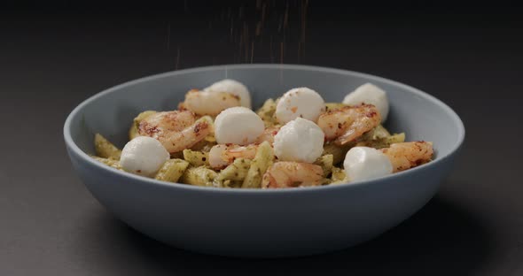 Slow Motion Seasoning Pesto Penne with Shrimps and Mozzarella in Blue Bowl on Black Background