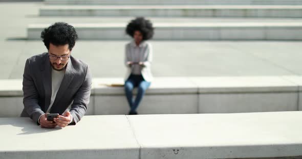 Businessman using smartphone at train station with woman in background