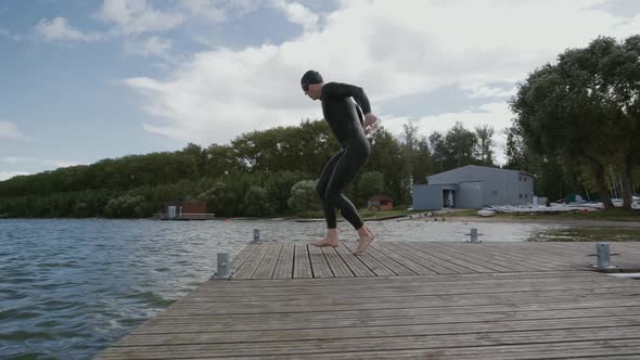 Triathlete in a Wetsuit Swims Runs and Jumps Into Open Water an Athlete Trains Before a Triathlon