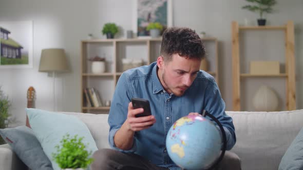 Young Man Buying Tickets Using Smartphone for Vacation at Home in Living Room