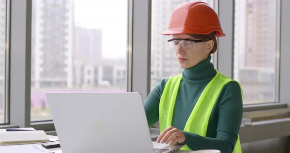 Women working on a laptop in a construction helmet. Woman engineer in the office uses a computer.