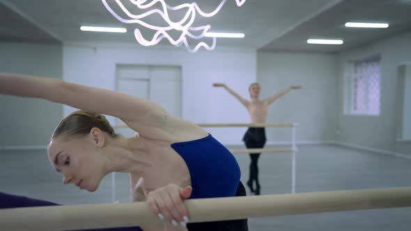 Portrait of Young Slim Caucasian Ballerina Bending and Stretching Raising Leg Up at Barre in Dance