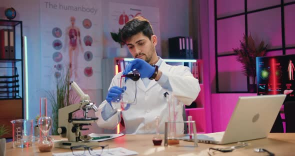 Chemist in white Coat and Gloves Working with Chemical Liquids and Glass Flasks