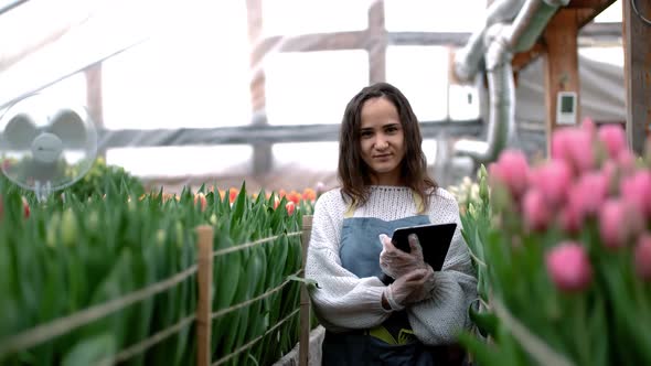 Portrait of a Beautiful Young Smiling Woman Florist in an Apron Stands with a Clipboard in a