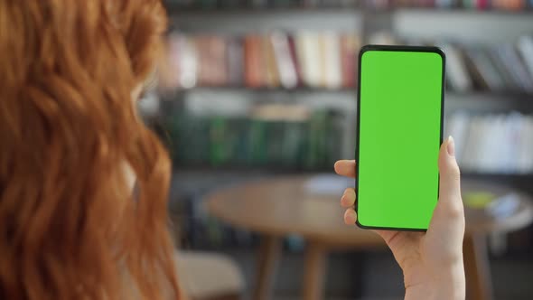 Back View of Young Woman at Home Office Sitting on Library Collage With Green Mockup Screen alt