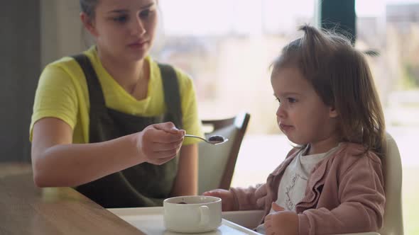 Closeup Mom Feed Young Baby in White Feeding Up High Chair Kid is Trying to Eat Himself Happy Child