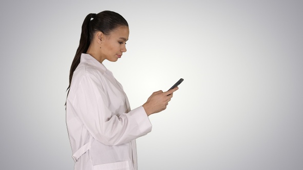 Cheerful cute young woman doctor typing text on phone while