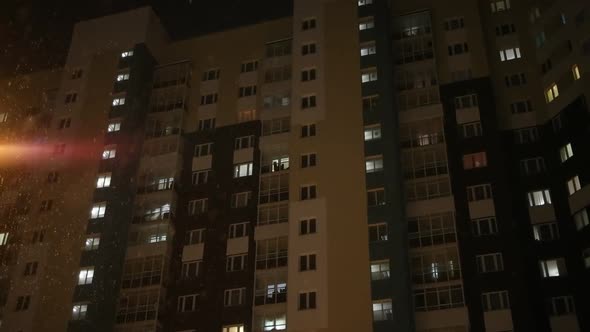 Snowfall in the Evening Against the Background of the Windows of an Apartment Building