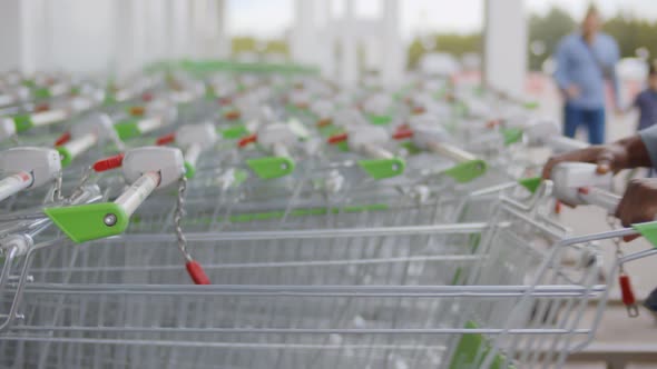 Close Up of African Man Shopper Pulling Shopping Cart From Row in Supermarket or Grocery Store.