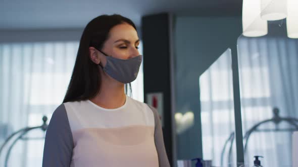 Caucasian female receptionist wearing face mask at hotel reception desk