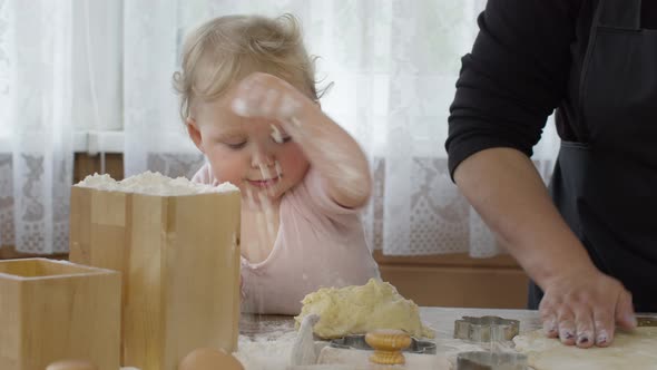 Baby Granddaughter Helps Granny Mixing Dough for Pastry and Puts Flour Close-up