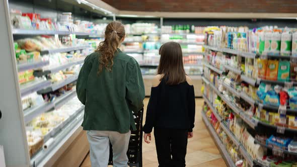 Teen Girl and Her Mom Shopping in the Supermarket with Cart Rear View