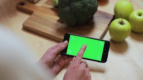 Closeup of Woman's Hand Browsing Smartphone with Chroma Key on Kitchen at Home. Breakfast Browse