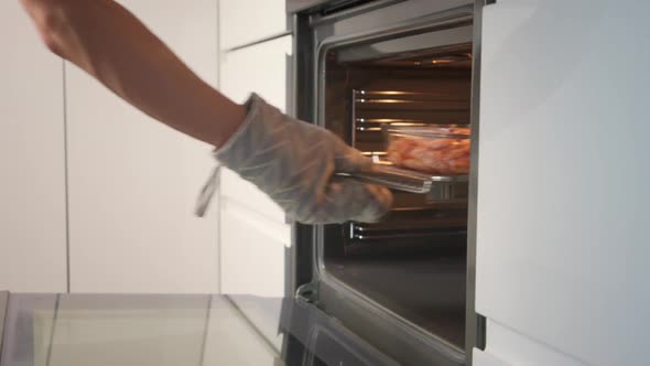 Hand in Potholder Opens Oven Door and Take Off Glass Dish