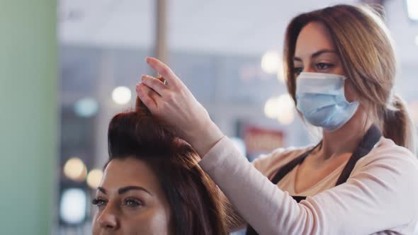 Female hairdresser wearing face mask putting rollers on hair of female customer at hair salon
