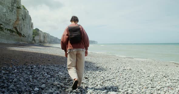 A Young Woman Walks Along a Pebbly Beach Past Sheer Chalk Cliffs