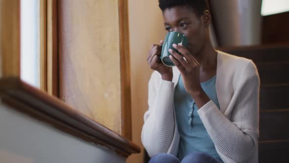 Thoughtful african american attractive woman sitting on stairs, drinking coffee