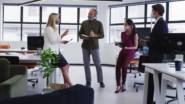 Diverse business colleagues wearing face masks having casual meeting standing in office